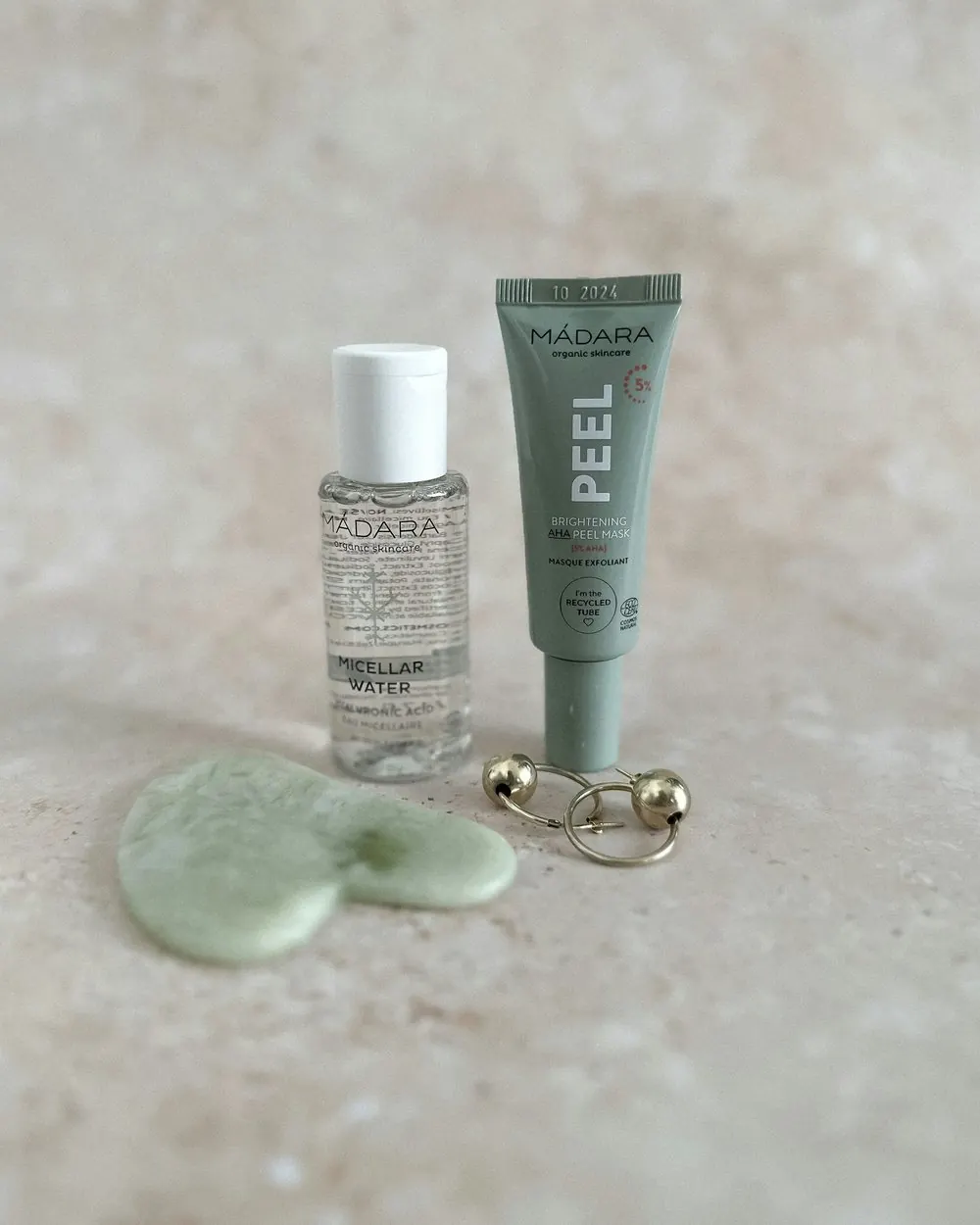 Skincare essentials and a jade gua sha on a stone surface